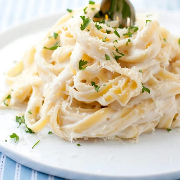 Creamy fettuccine alfredo with parsley and grated cheese, with a fork in the pasta.