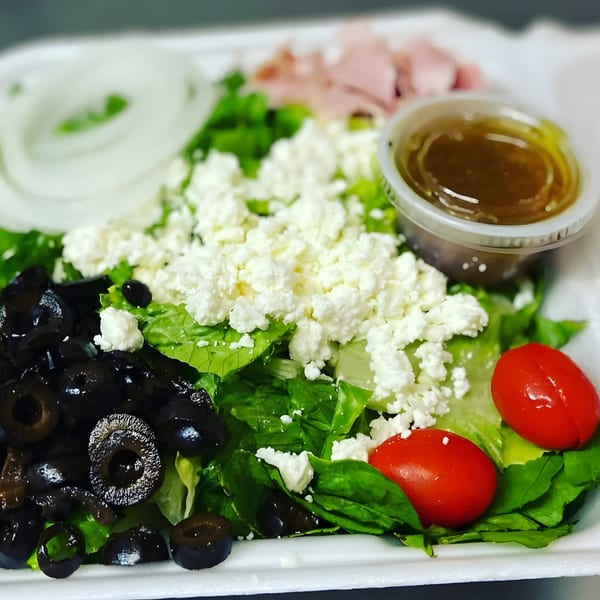 Fresh garden salad with lettuce, feta, olives, tomatoes, onions, ham, and dressing from Brooklyn's Pizzeria.