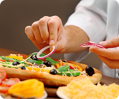 A person cutting vegetables on top of a pizza.